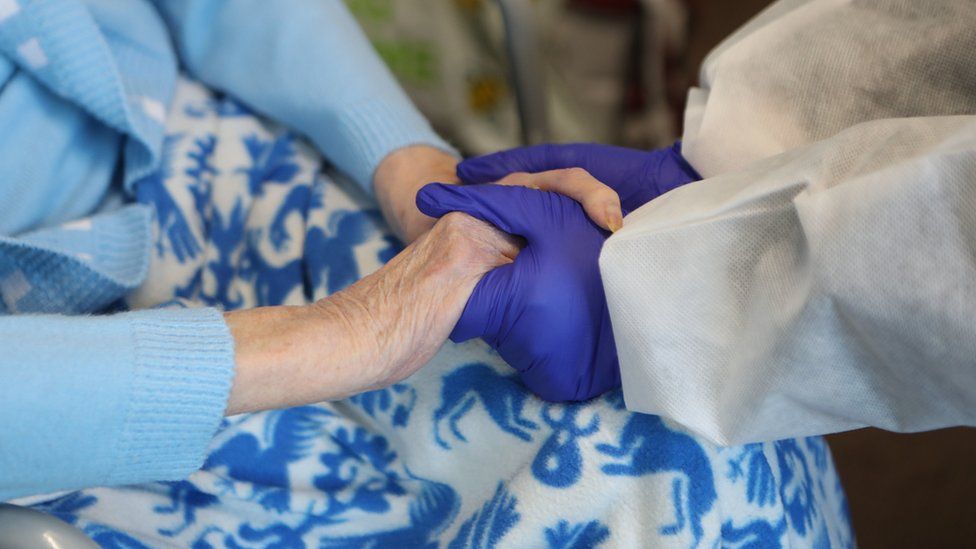 Elderly woman holding hands with carer wearing PPE
