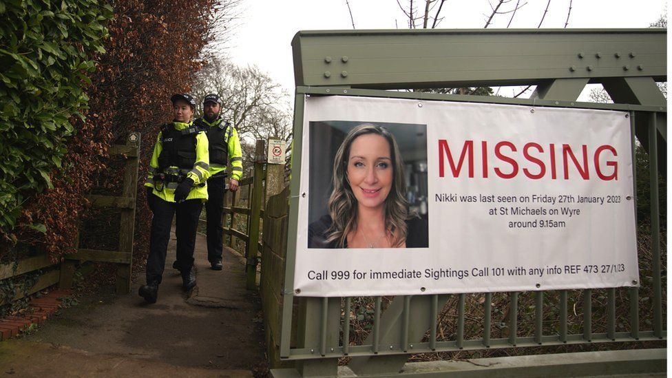 Police officers walk by a poster appealing for information about the disappearance of Nicola Bulley, on a bridge over the River Wyre