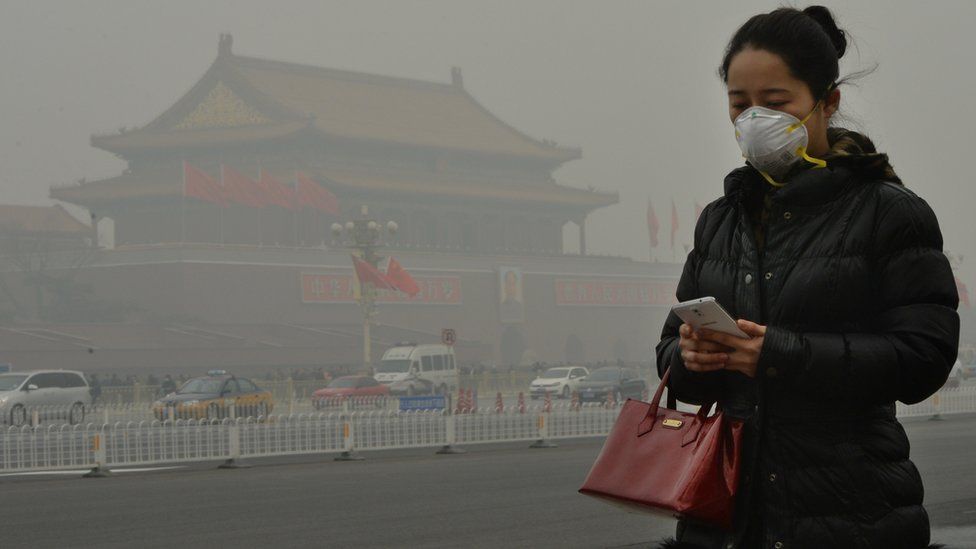 A woman walks beside Tiananmen Square as heavy air pollution continues to shroud Beijing on 26 February 2014