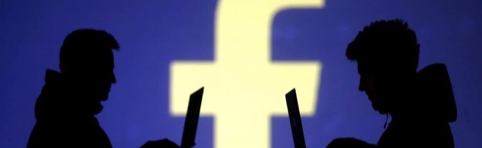 Silhouettes of laptop users are seen next to Facebook logo. File photo
