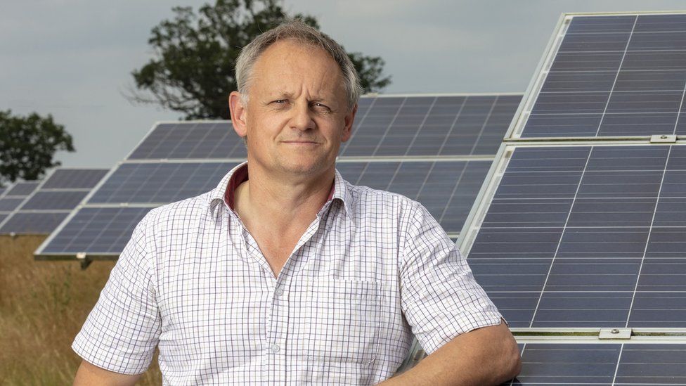 Andrew Blenkiron stands with his arm on a solar panel on his farm