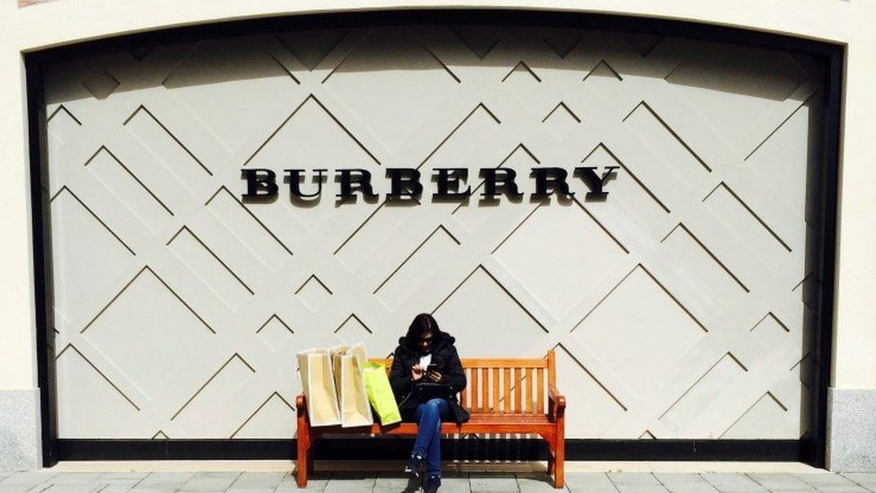 A woman sits in front of a Burberry store