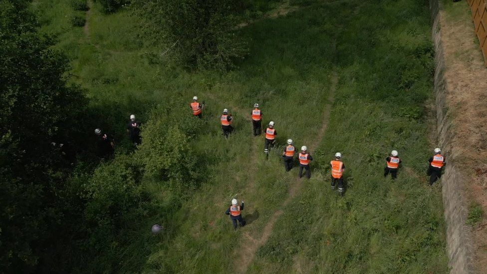 A drone shot of volunteers from the Community Rescue Service fanned out in a line searching long grass