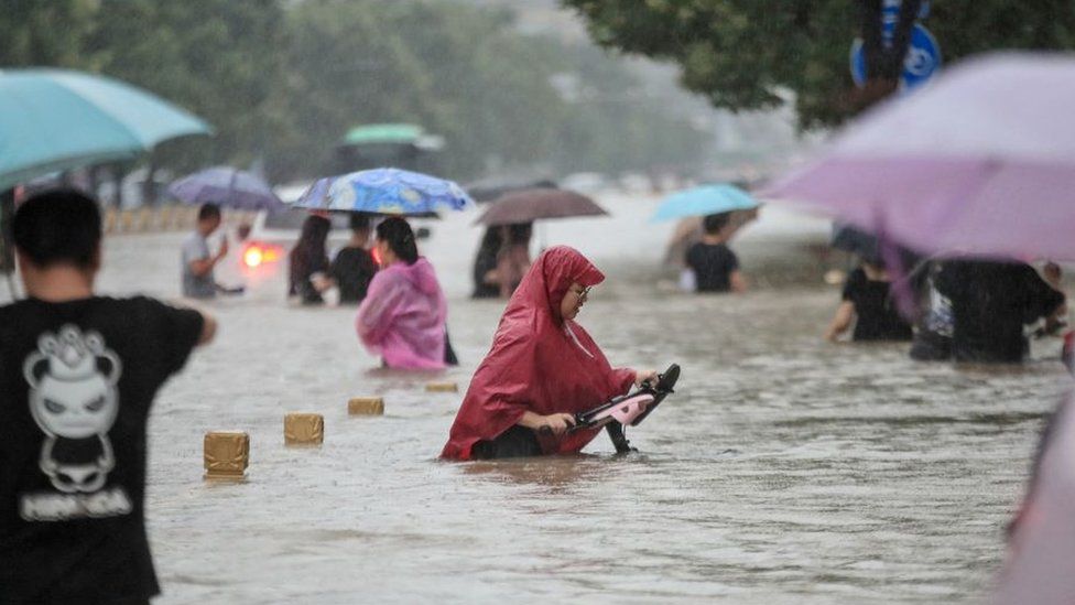 This photo taken on July 20, 2021 shows people wading through flood waters along a street following heavy rains in Zhengzhou