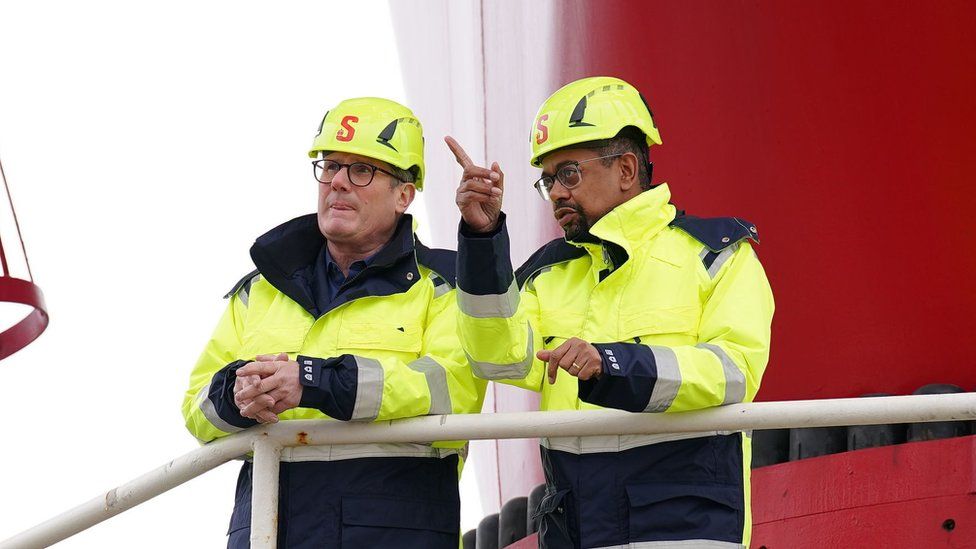 Keir Starmer and Vaughan Gething, both on hard hats and and high visibility jackets on a wind turbine platform
