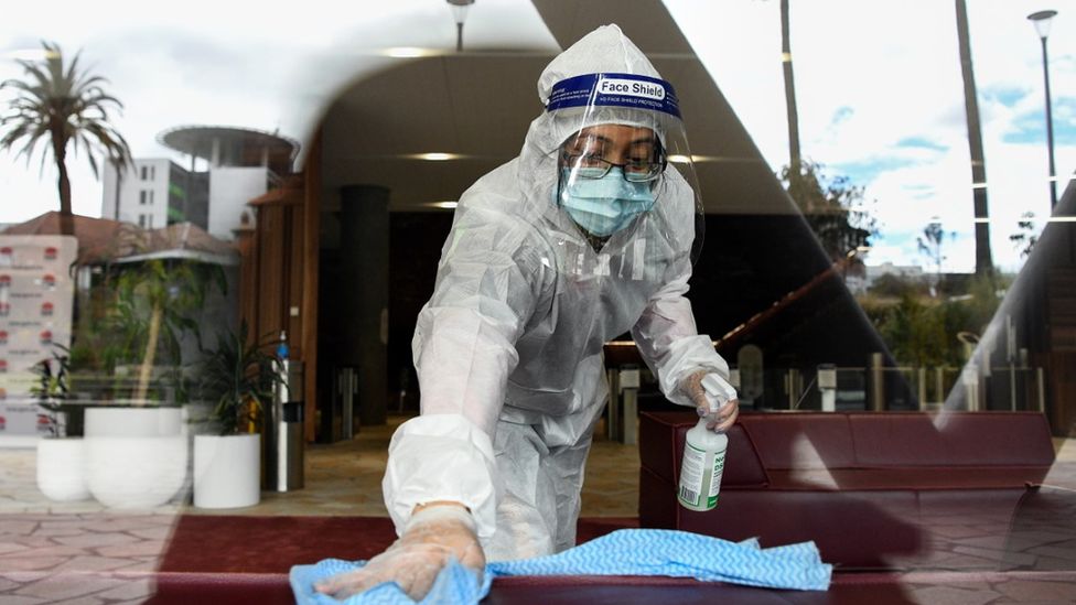 A cleaner in full protective uniform wipes down a surface at a government health building in Sydney