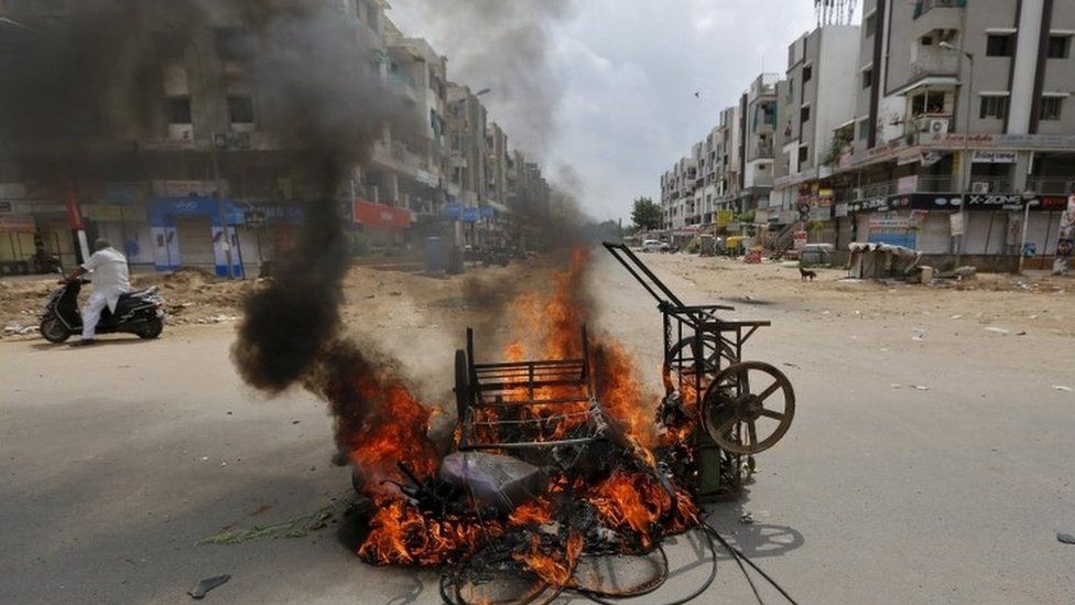 A man on a scooter stands next to burning vehicles after the clashes between the police and protesters in Ahmedabad, India, August 26, 2015.