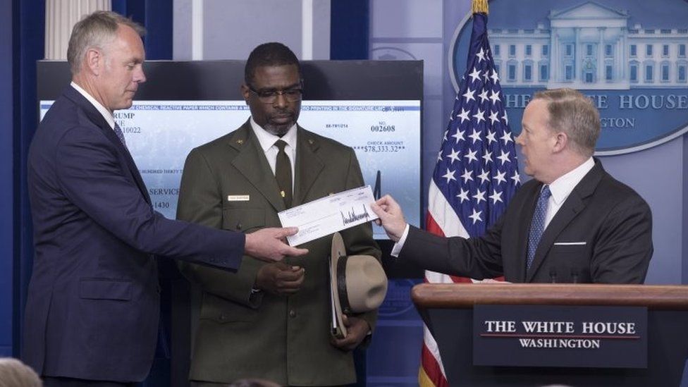 White House Press Secretary Sean Spicer (R) hands a check of funds being donated by US President Donald J. Trump (not pictured) to the National Park Service, to US Interior Secretary Ryan Zinke (L) and Tyrone Brandyburg (C).