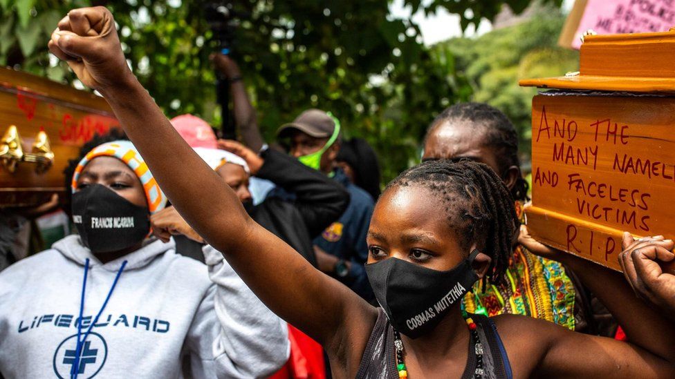 Cosmas Mutethia"s wife (R) wears a mask with her husband"s name, who was killed by Kenyan Police during a night curfew, as she carries an empty coffin during their protest against police brutality in front of the Kenyan Parliament in Nairobi on June 9, 2020.