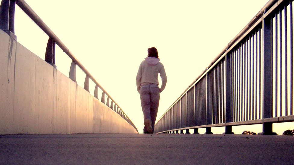 A stock model walks across a bridge with her back to the camera