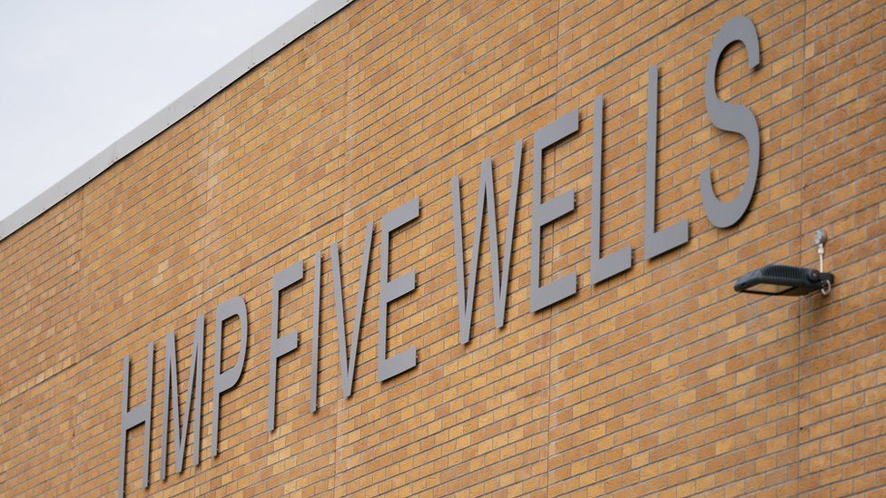 Brick wall of prison with "HMP Five Wells" lettering