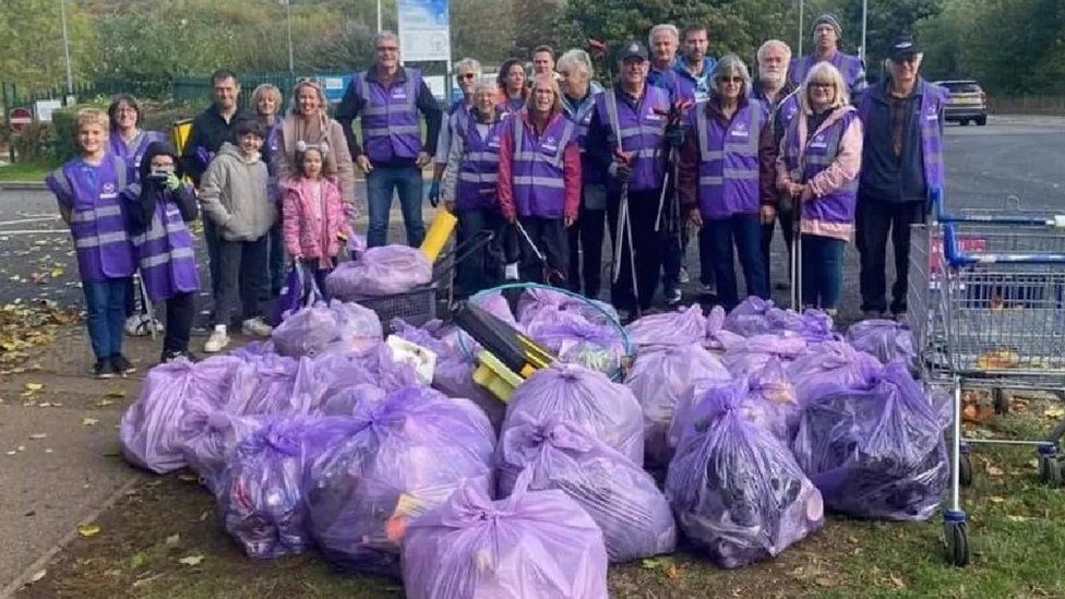 Group of people in purple hi-viz jackets standing behind purple bags of rubbish