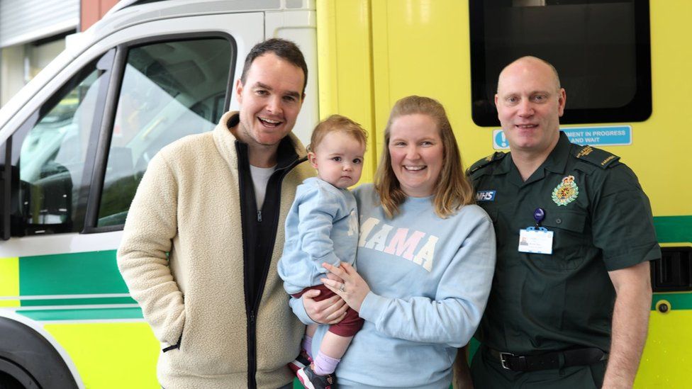 Tim, baby Cecilia, Alex and paramedic Mike Sage standing next to an ambulance