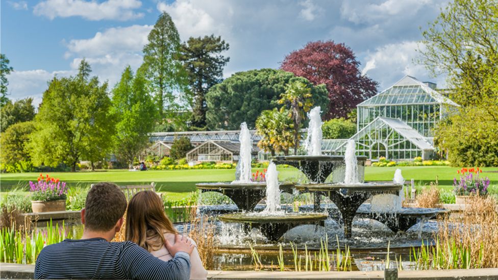 View of Cambridge University Botanic Garden with fountain, glass house and people