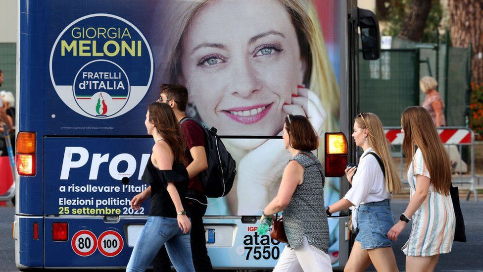 People walk a by an election poster showing Giorgia Meloni, leader of the 'Partito Fratelli D'Italia' , with the slogan "Ready to raise Italy"