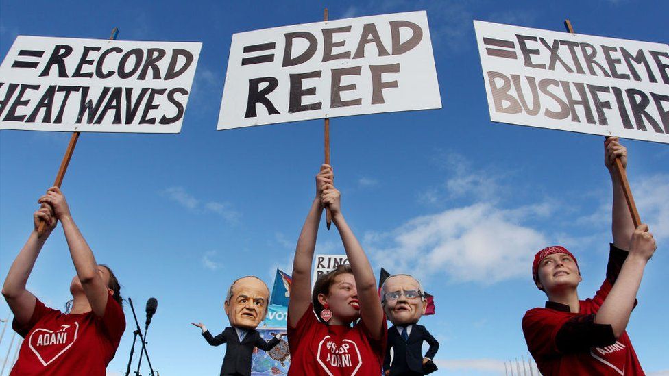 Молодые активисты-экологи держат плакаты протеста перед комиками в костюмах лидера лейбористов Билла Шортена и премьер-министра Скотта Моррисона 5 мая 2019 года в Канберре, Австралия
