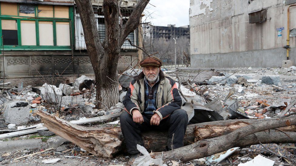 A local resident sits near a damaged apartment building in Mariupol