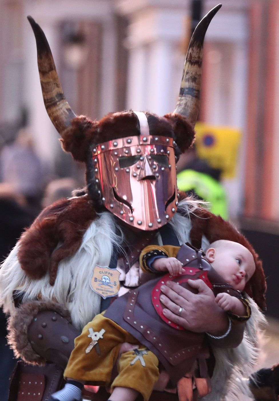 Reveller dressed as a warrior walks through Lewes carrying a baby