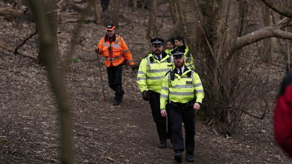 Police and a search volunteer in woods near Brighton