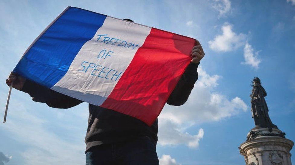 A protester waves a French Tricolor flag with 'Freedom of Speech' written on it during an anti-terrorism vigil on Sunday