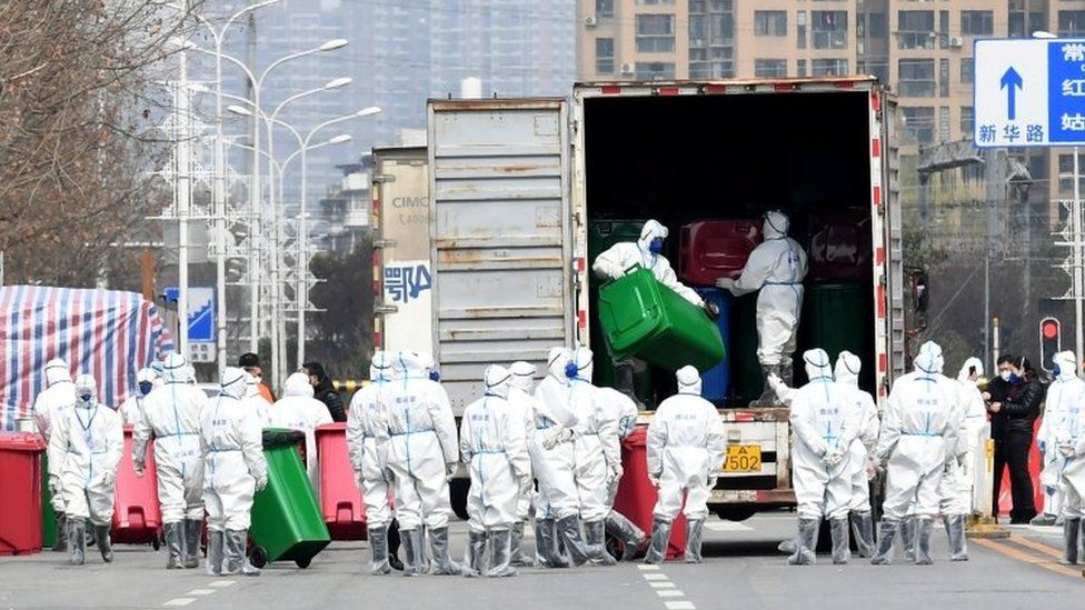 Рабочие в защитных костюмах разгружают мусорные баки во время дезинфекции на рынке морепродуктов Хуанань в Ухане. Файл фото