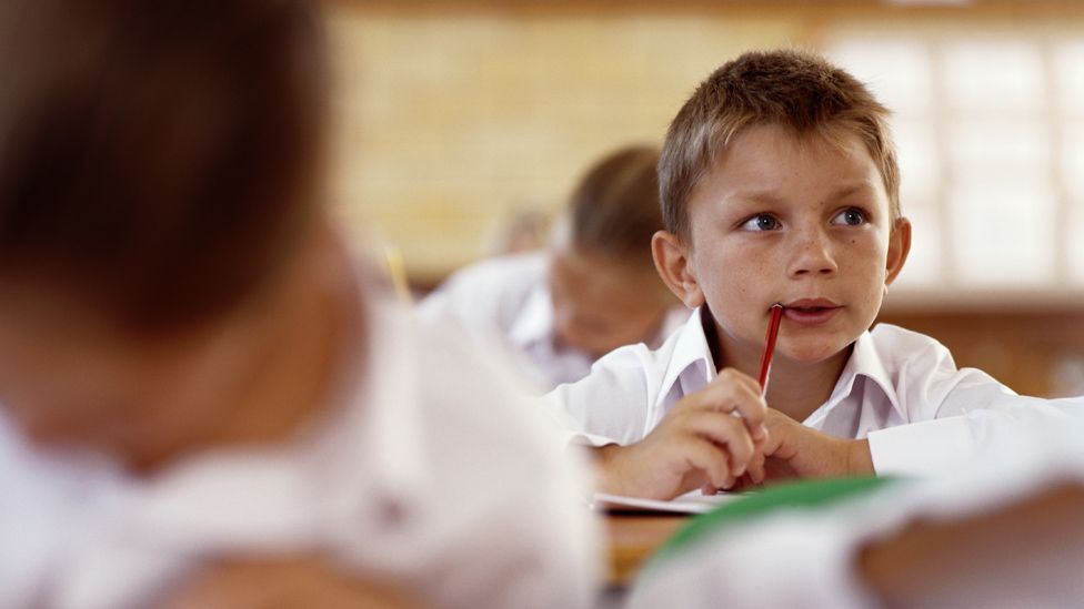 Boy in a classroom, holding pen to mouth