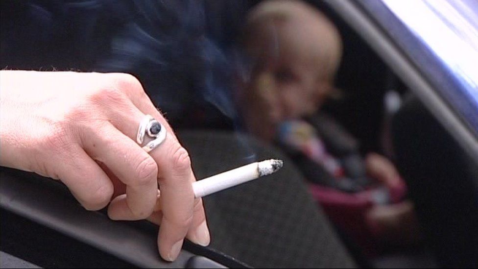 Smoker holding cigarette beside child in vehicle