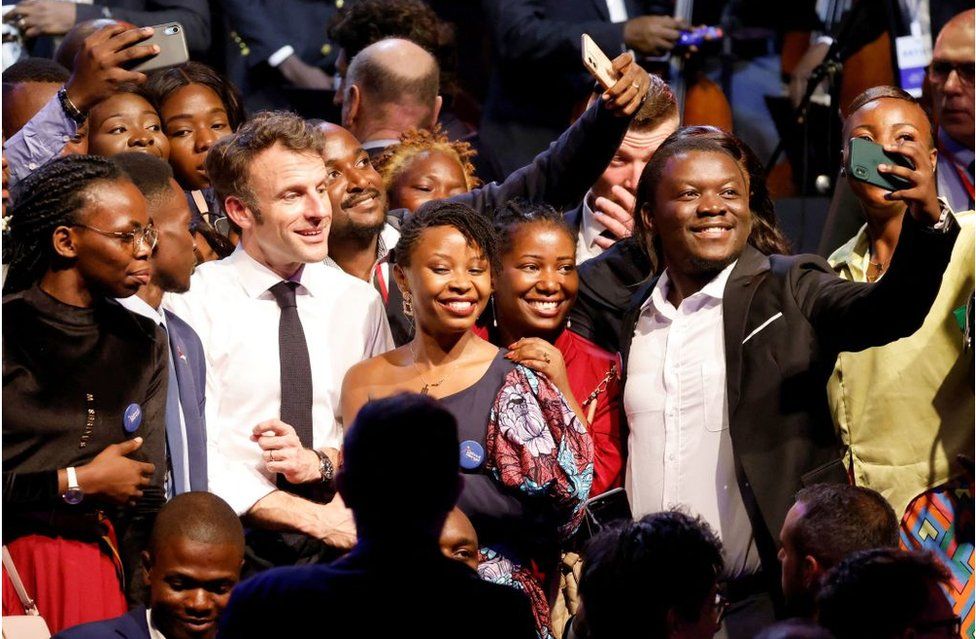 President Macron posing for selfies with smiling guests in Kinshasa.