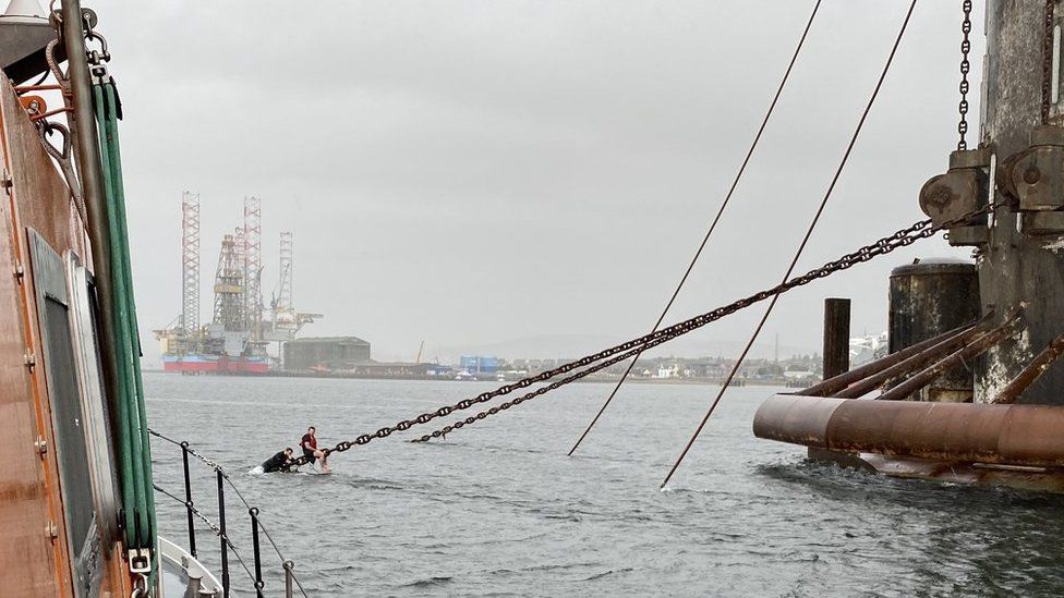 Men clinging to rig anchor chain