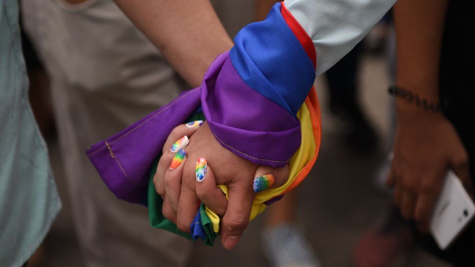 A couple holds hands wrapped in a rainbow flag