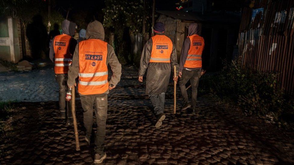 Four patrol officers wearing orange fluorescent overcoats with sticks in their hands