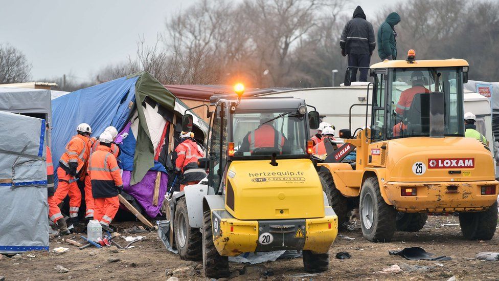 Agents and bulldozers dismantle shacks as two people stand on a caravan"s roof on March 1, 2016 in the "Jungle" migrant and refugees camp in the French northern port city of Calais.