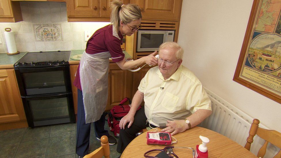 Nurse takes temperature of Sean Daly in his kitchen