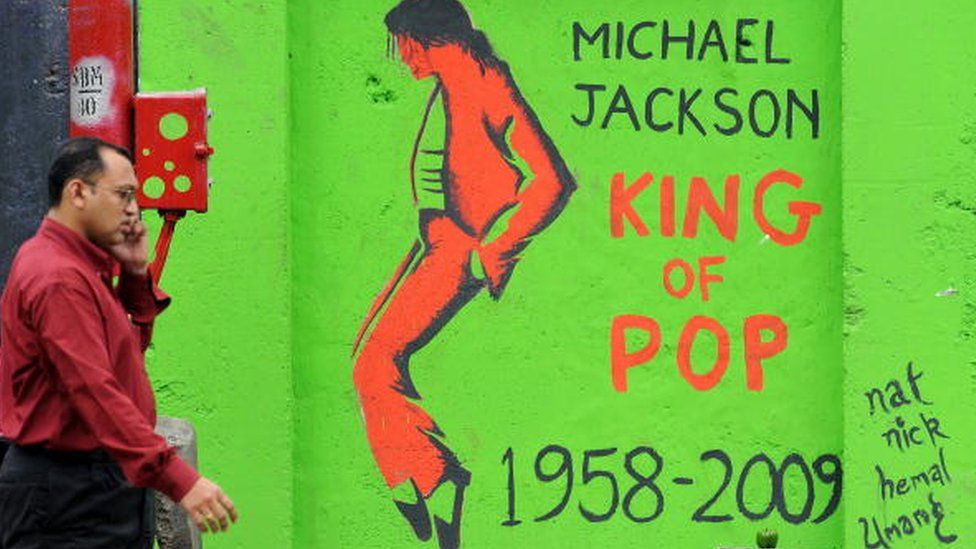 An Indian pedestrian speaks into a cellular telephone as he walks past a grafitti image of the late "King of Pop" Michael Jackson on a wall in Mumbai on August 28, 2009,