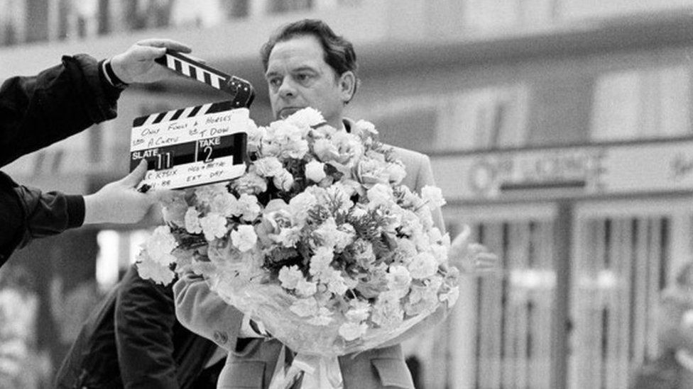 Black and white photo of David Jason carrying a huge bunch of roses