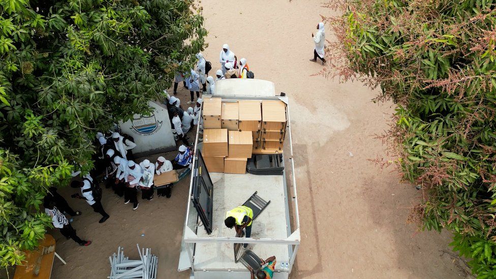 A birds-eye view of a truck with office cabinets on a sandy road surrounded by people.