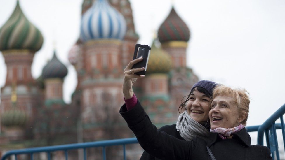 Two women take a selfie in front of St Basil's Cathedral in Moscow