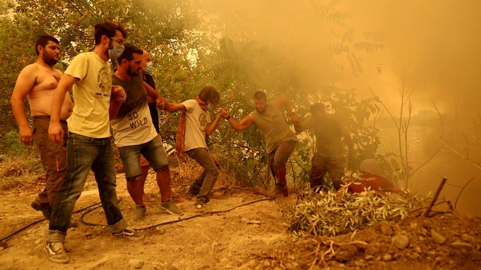 Мужчине, держащему шланг, помогают подняться по склону, когда горит лесной пожар в деревне Гувес на острове Эвия, Греция, 8 августа 2021 г.