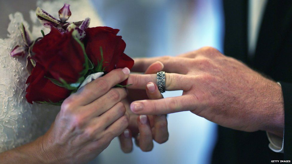 Luanne Round slips a ring on the finger of her husband Matthew Round as they are wed during a group Valentine"s day wedding at the National Croquet Center on February 14, 2013 in West Palm Beach, Florida.