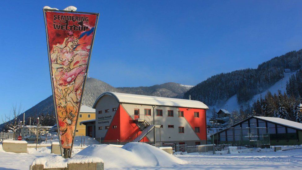 A triangular banner featuring the nude painting is seen displayed outside resort buildings in snowy Semmering