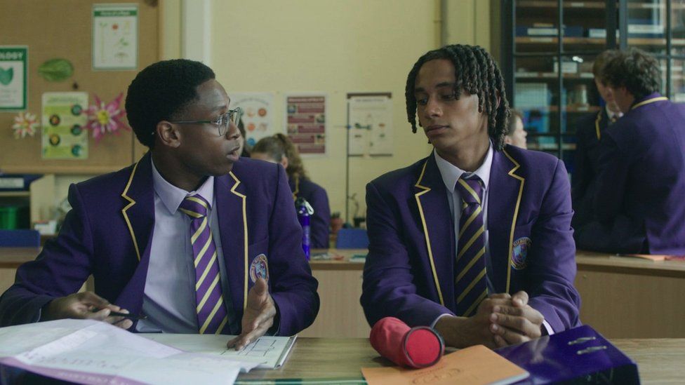 Production still of Myles Kamwendo (L) and Sekou Diaby in scene from BBC Three drama series Boarders. They are sat next to each other in a classroom.