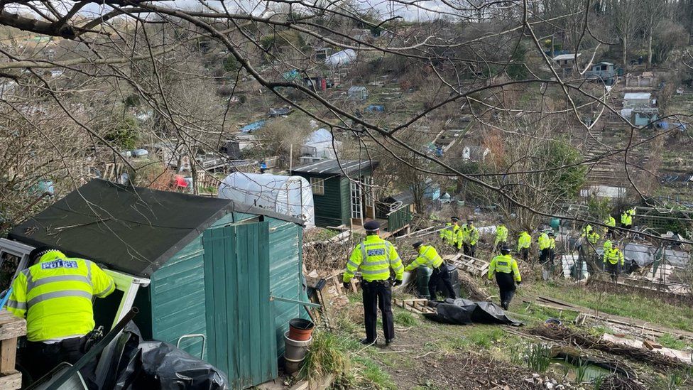 Around 20 Metropolitan Police officers walking in a line through the Roedale Valley allotments north of Stanmer Villas