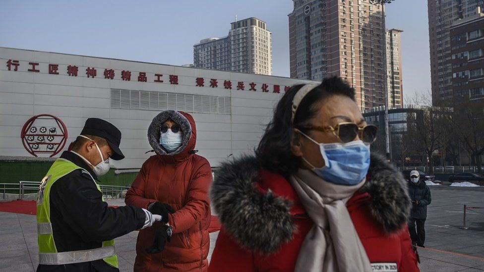 A Chinese woman (left) wears a protective mask as she has her temperature checked by an official entering a park on 9 February 2020 in Beijing, China