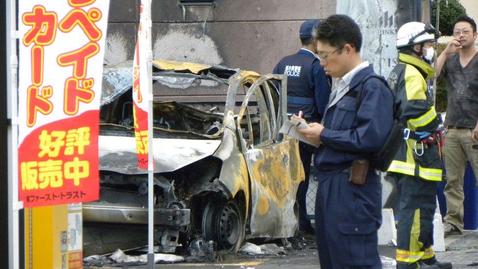 Police investigate a nearby burned out car which caught fire at the same time as the explosions