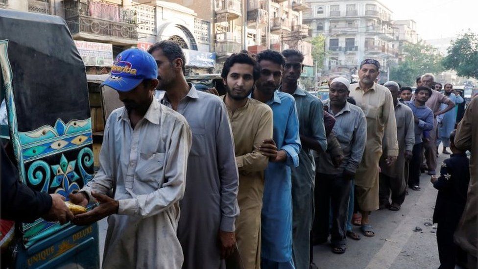 People stand in queue to receive charity food handout, during the fasting month of Ramadan, along a road in Karachi, Pakistan March 30, 2023.
