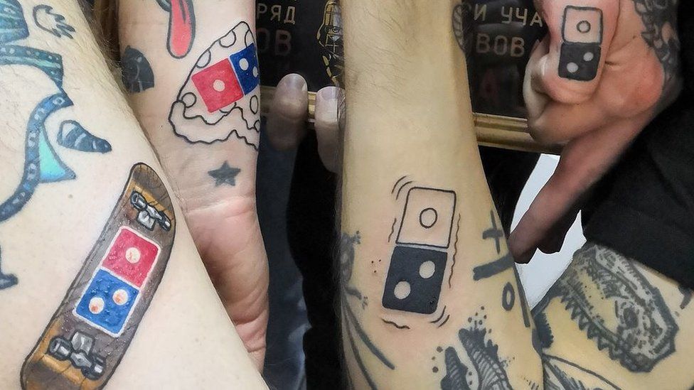 Four people pose with their domino's tattoos.
