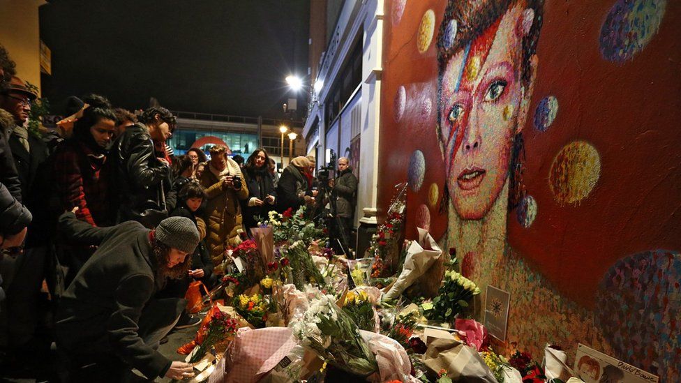 A woman leaves flowers beneath a Jimmy C mural of David Bowie in Brixton on January 11, 2016 in London