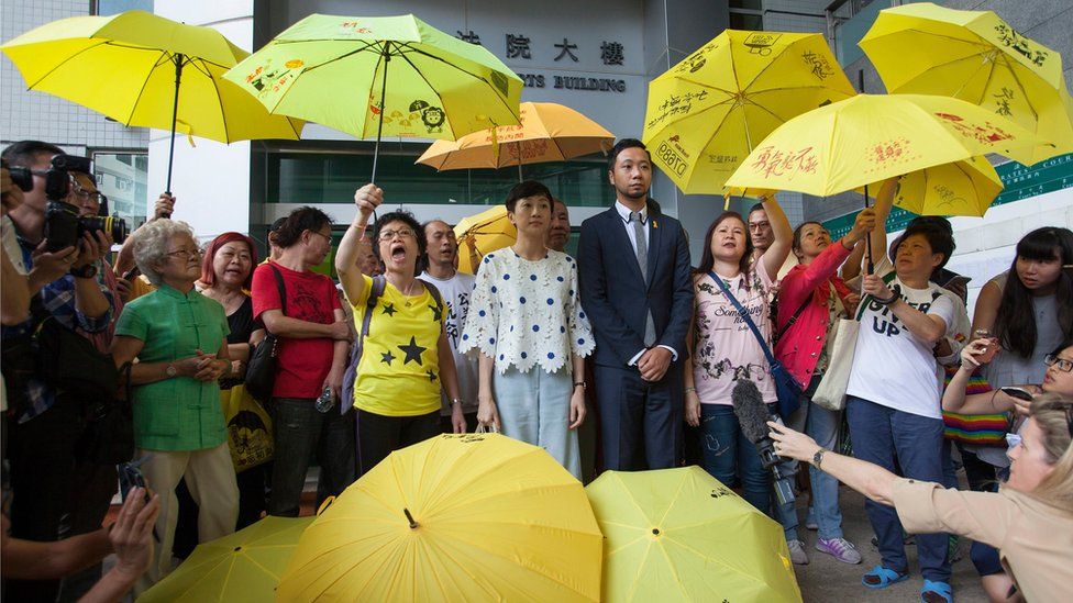 Pro-democracy activist Ken Tsang (centre-right, in a suit) outside Kowloon City Magistrates Court, with a crowd of supporters, many of them carrying yellow umbrellas, before entering court for his trial, on 26 May 2016, in Hong Kong.