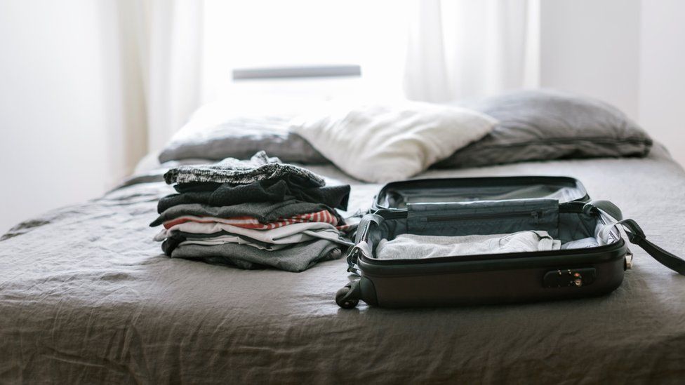 An open suitcase and a pile of folded clothes on a hotel bed.