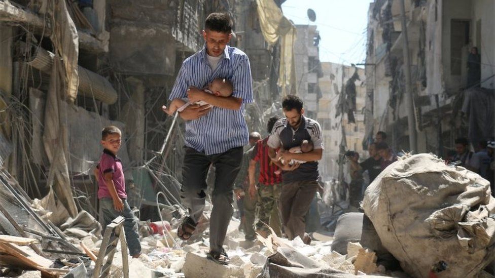 Syrian men carry babies through rubble in Salihin neighbourhood of Aleppo (September 2016)